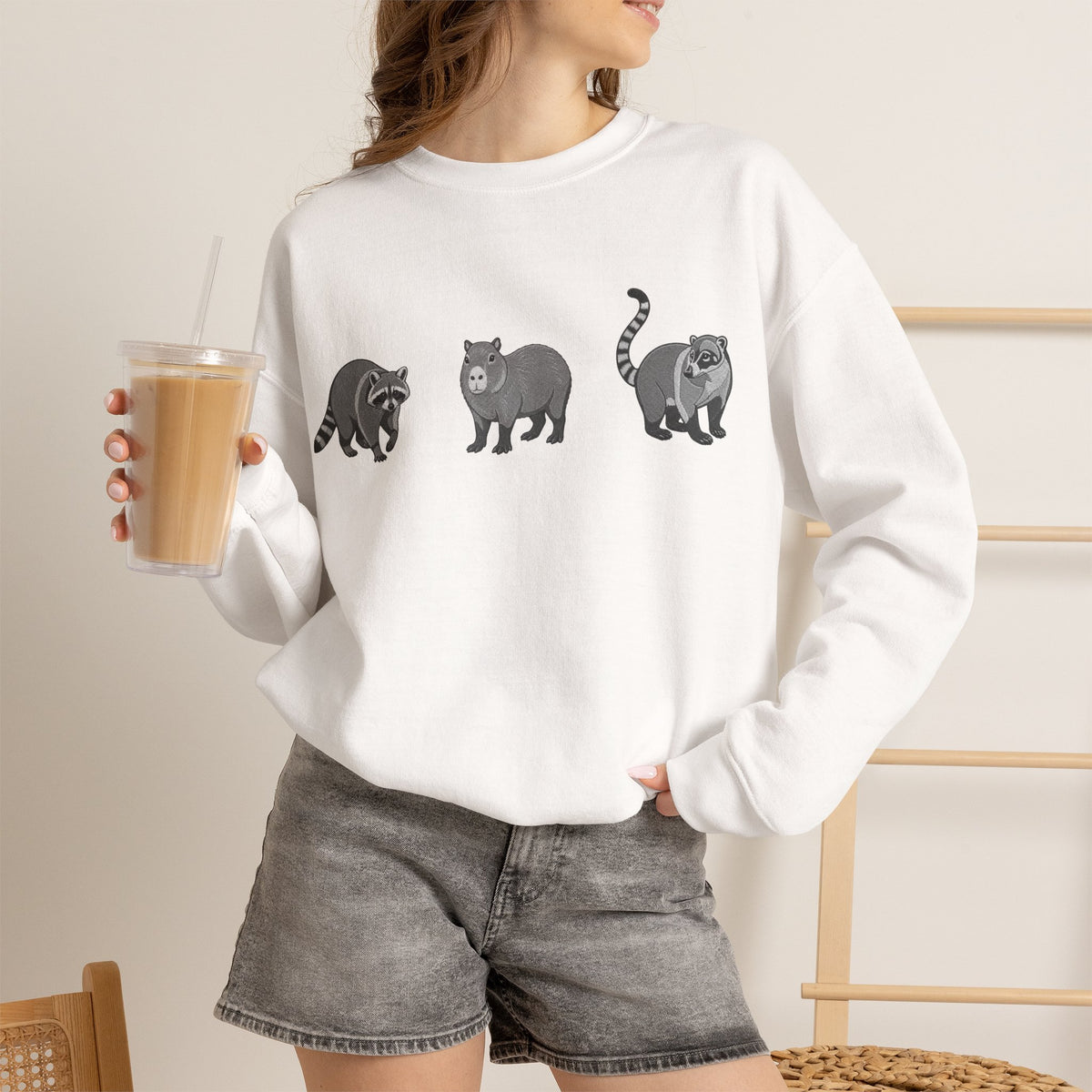 Wildlife Trio graphic sweatshirt featuring raccoon, capybara, and coati designs from Wyldelife Collection by Printify.