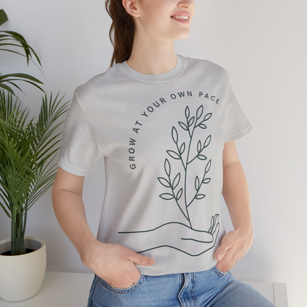 Minimal botanical print T-shirt with "Grow At Your Own Pace" slogan, featuring green leafy design on a casual Printify tee.