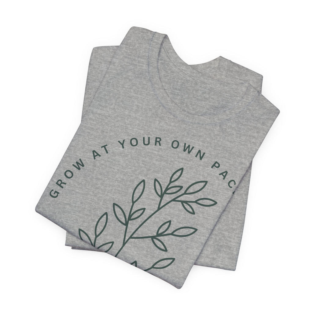 Minimal botanical design T-shirt with "Grow At Your Own Pace" slogan by Printify, featuring green plant illustrations on soft fabric.