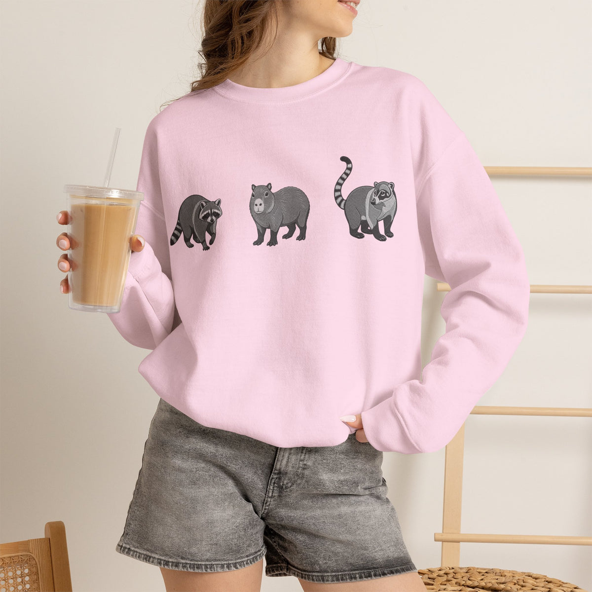 Wildlife Trio graphic sweatshirt featuring raccoon, capybara, and coati illustrations from Wyldelife Collection by Printify.
