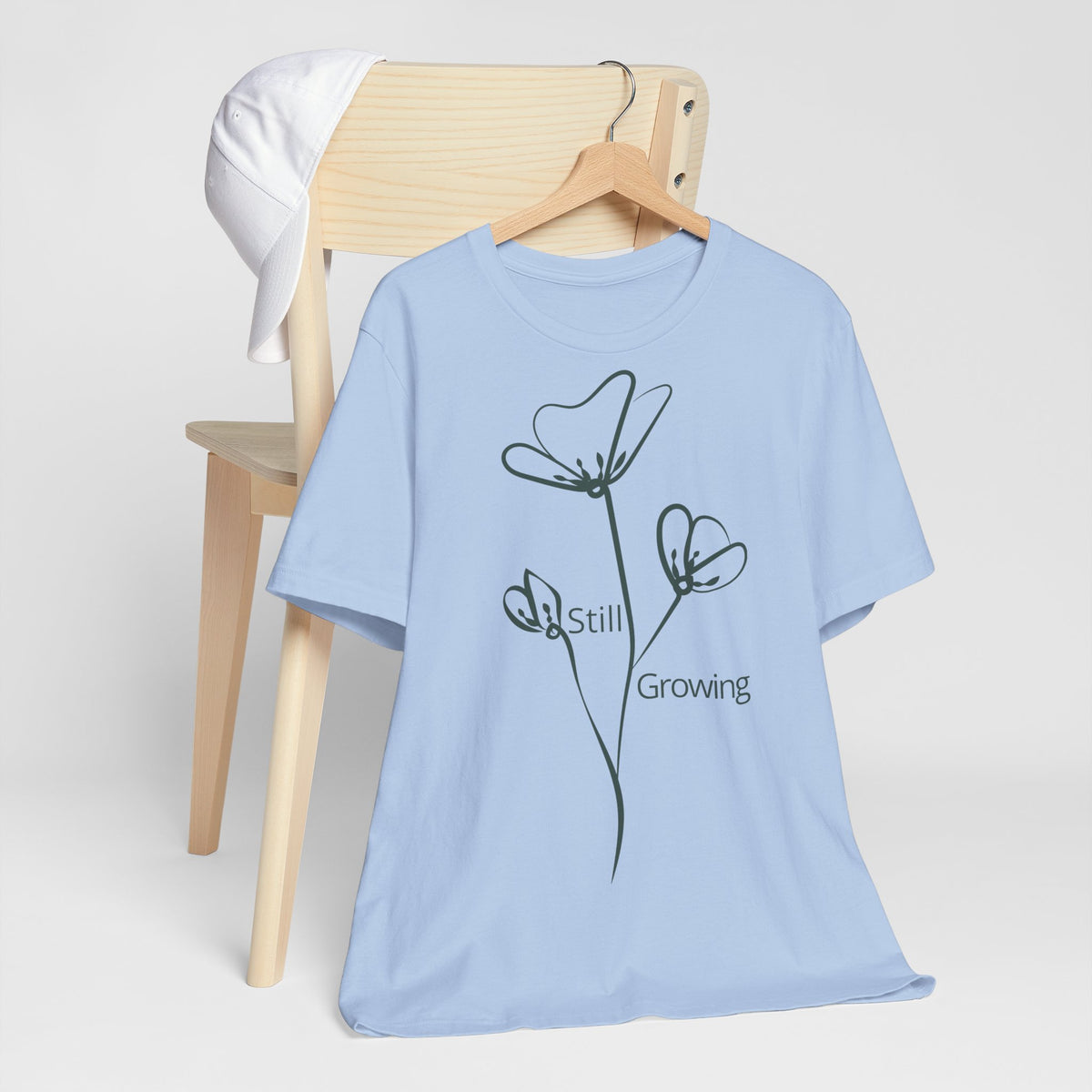 Still Growing Floral T-Shirt by Printify featuring a minimalist floral design and inspirational message on a comfortable cotton tee.