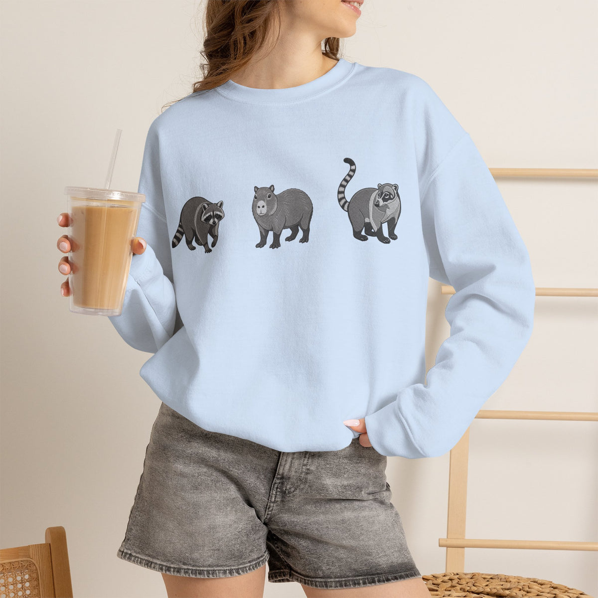 Wildlife Trio graphic sweatshirt featuring raccoon, capybara, and coati from Wyldelife Collection by Printify.