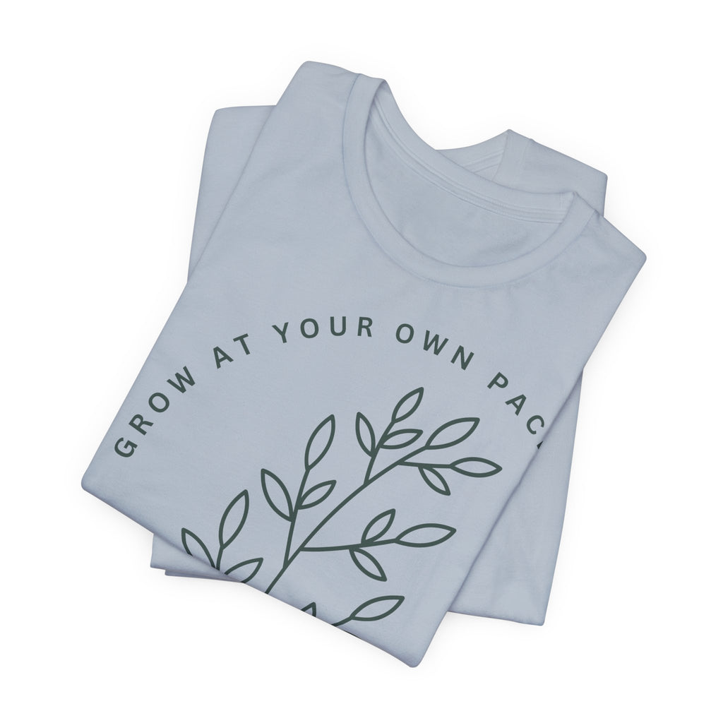 Minimal botanical T-shirt from Printify featuring "Grow At Your Own Pace" slogan with green plant illustrations.