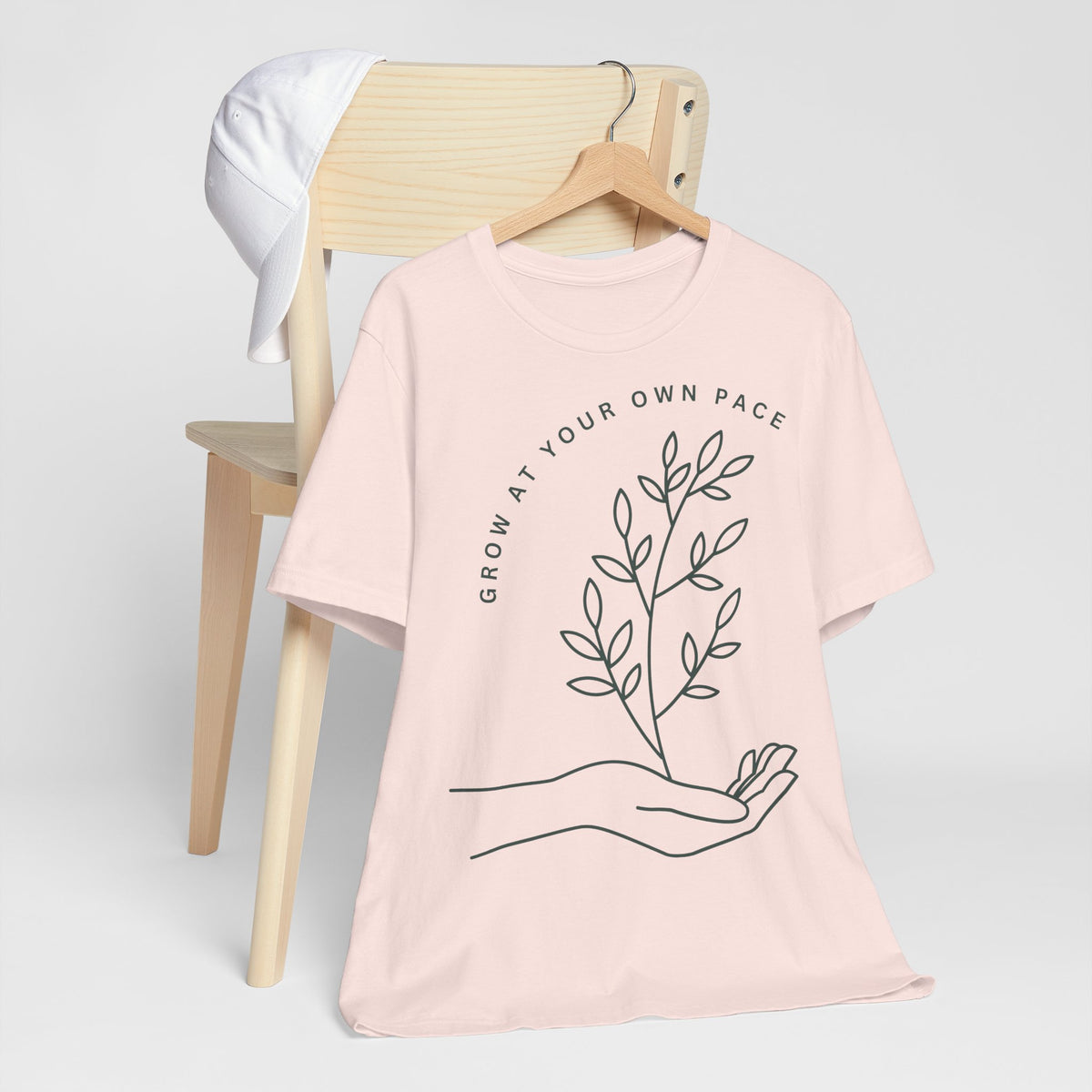 Minimal botanical print T-shirt with "Grow At Your Own Pace" slogan by Printify, featuring a simple green plant design.