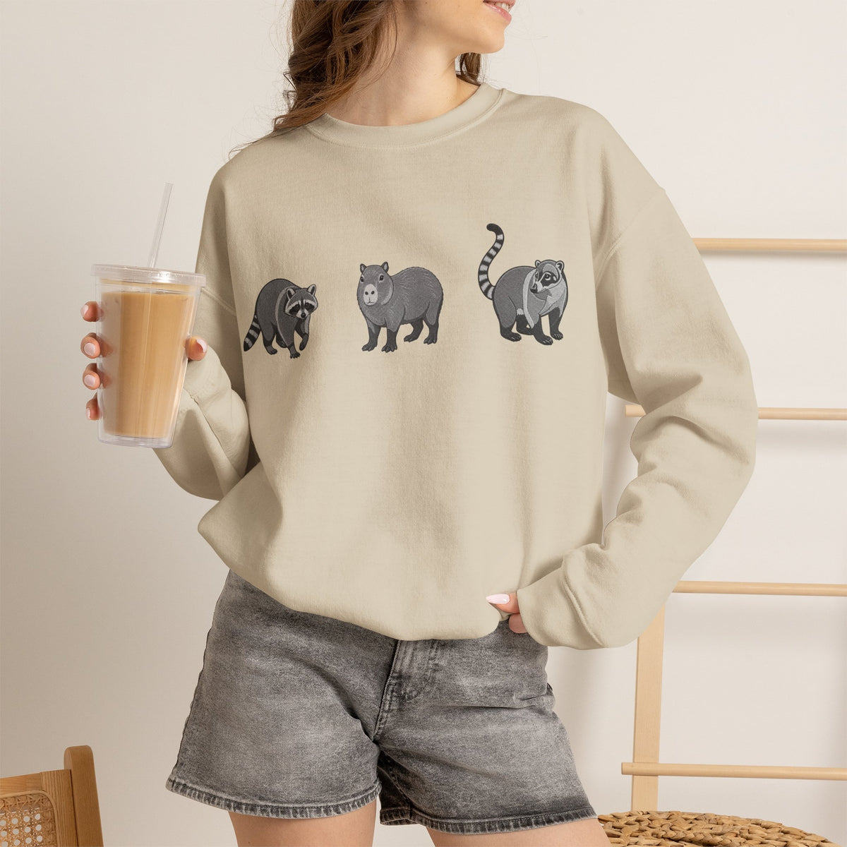 Wildlife Trio graphic sweatshirt featuring raccoon, capybara, and coati images from Wyldelife Collection by Printify.