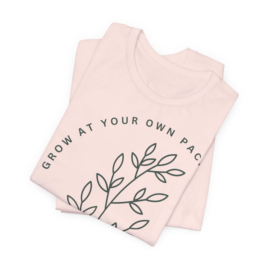 Minimal botanical T-shirt by Printify featuring "Grow At Your Own Pace" text, with green leaf illustrations on soft fabric.