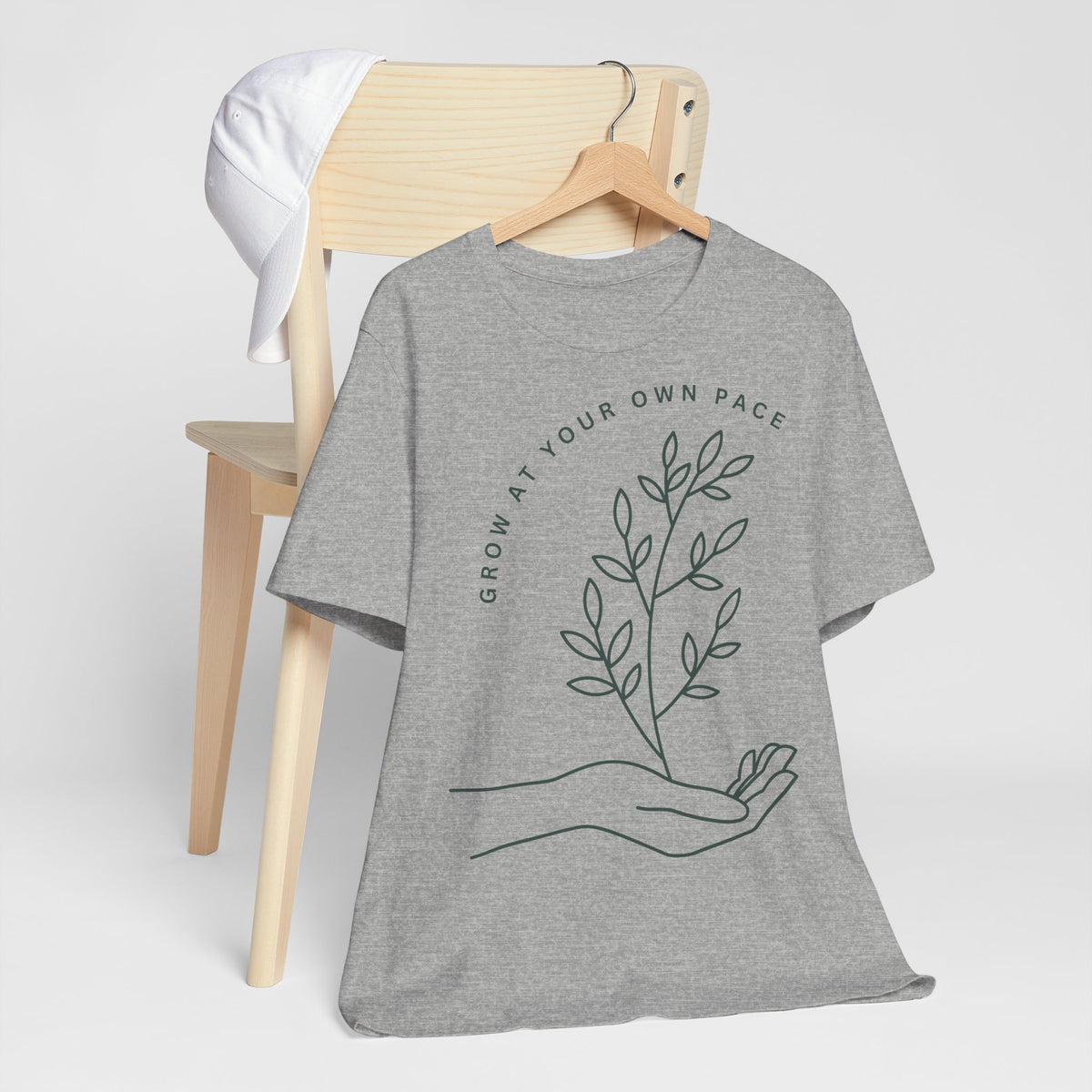Minimal botanical T-shirt with "Grow At Your Own Pace" quote, featuring green plant illustrations on a casual printify tee.
