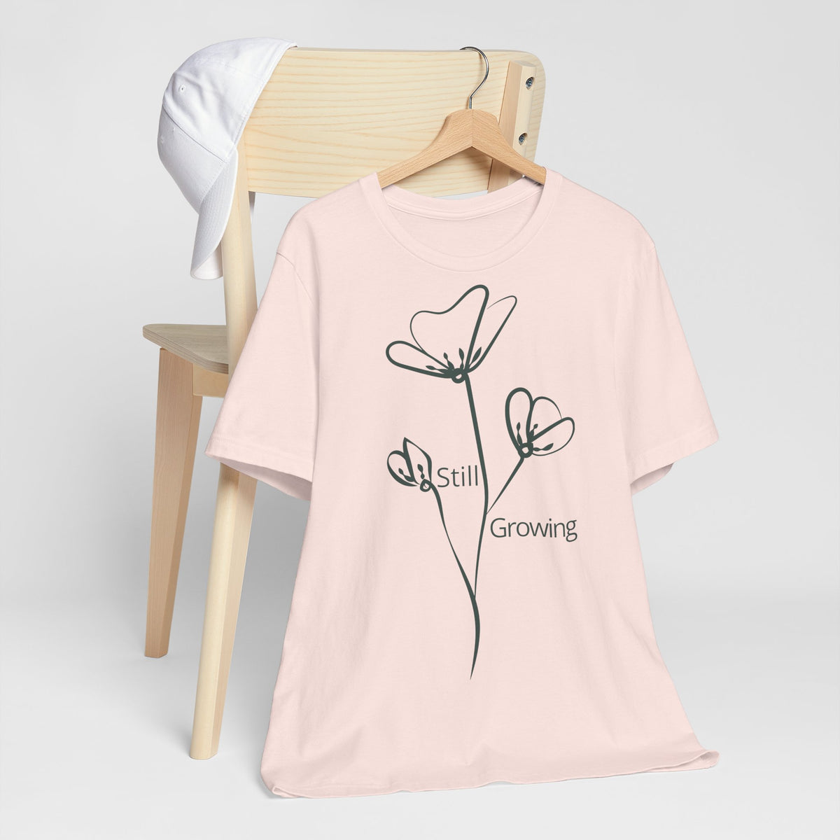 Still Growing floral T-shirt by Printify featuring a minimalist inspirational design, displayed on a white background.