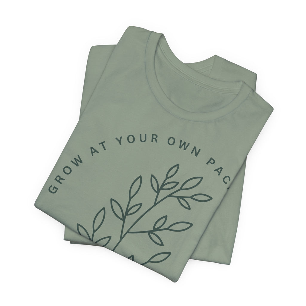 Minimal botanical T-shirt by Printify featuring "Grow At Your Own Pace" slogan and simple plant illustrations on soft fabric.