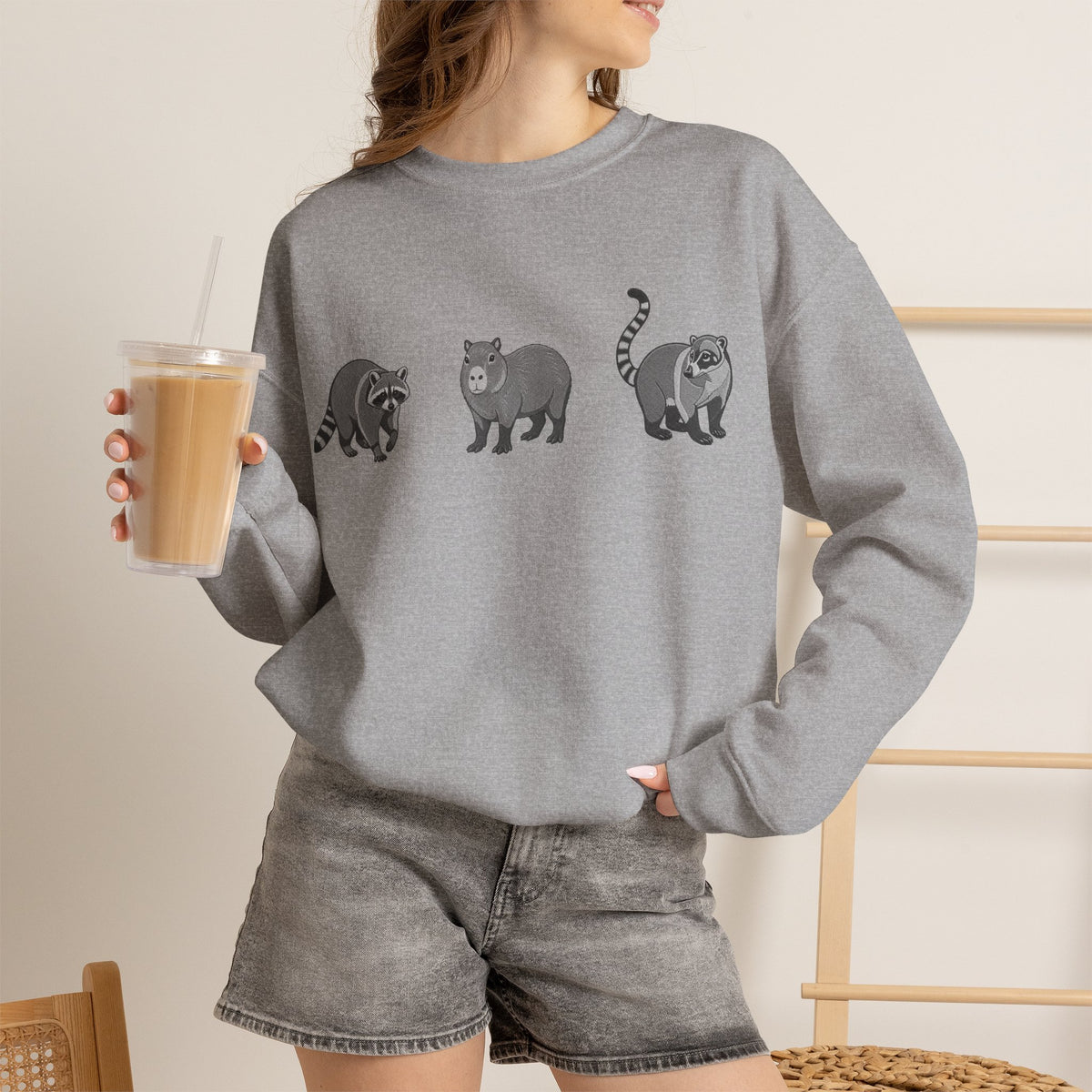 Wildlife Trio sweatshirt featuring raccoon, capybara, and coati graphic in the Wyldelife Collection by Printify