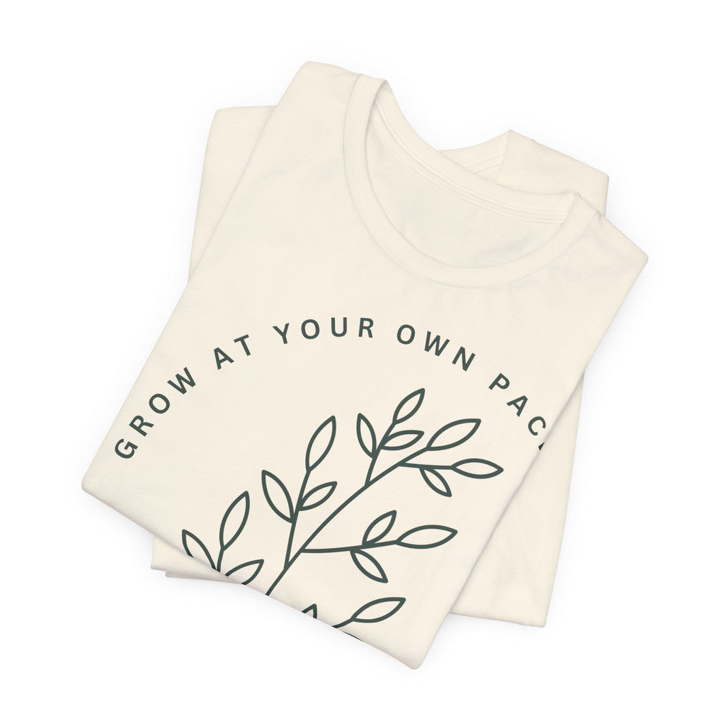 Minimal botanical print T-Shirt from Printify with "Grow At Your Own Pace" slogan, featuring green plant illustrations on soft fabric.