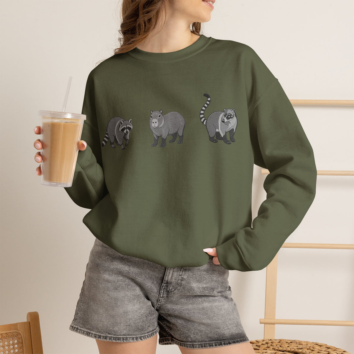 Wildlife Trio graphic sweatshirt featuring raccoon, capybara, and coati illustrations in Wyldelife Collection by Printify