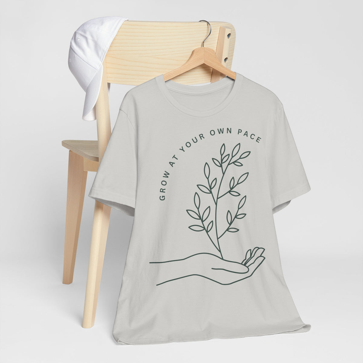 Minimal botanical print T-shirt with "Grow At Your Own Pace" slogan, casual fit, by Printify, featuring green plant illustrations.