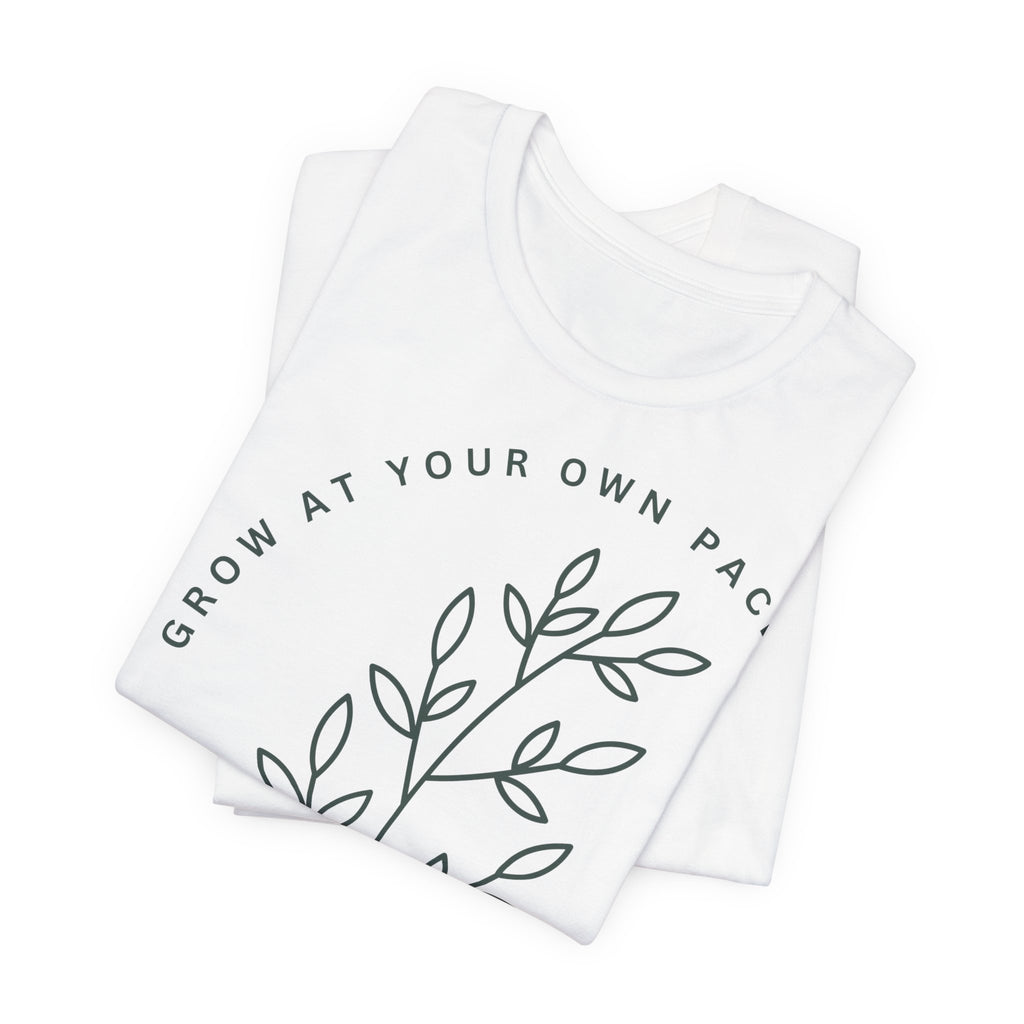 Minimal botanical print T-shirt from Printify with "Grow At Your Own Pace" slogan, featuring green plant illustrations on soft fabric.