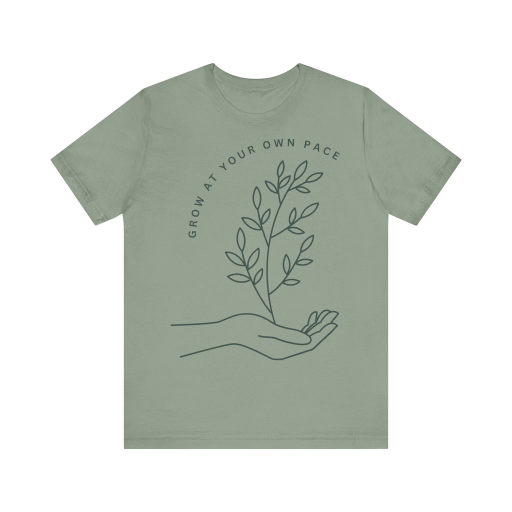 Minimal botanical print T-shirt with "Grow At Your Own Pace" slogan, featuring a green plant design on a casual tee.
